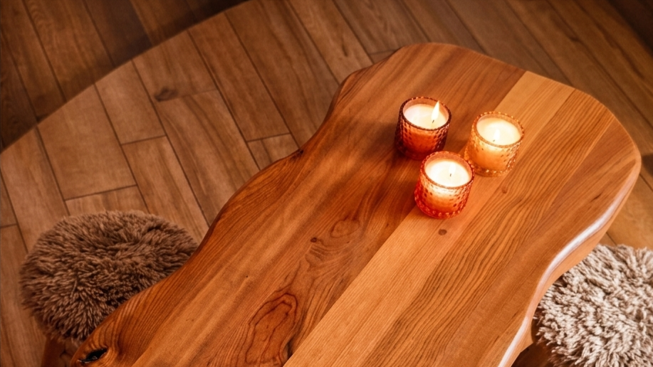 Wooden table with three candles and three fluffy stools on a wooden floor.